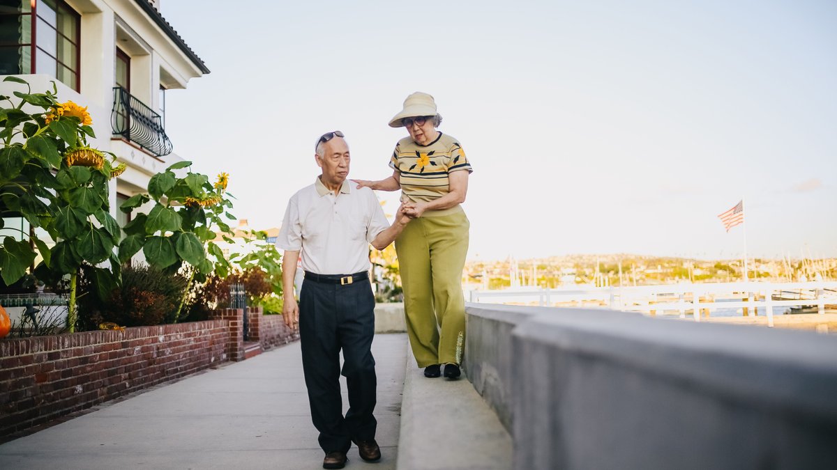 A senior Asian couple enjoys a walk outdoors on a sunny day, showcasing leisure and companionship.