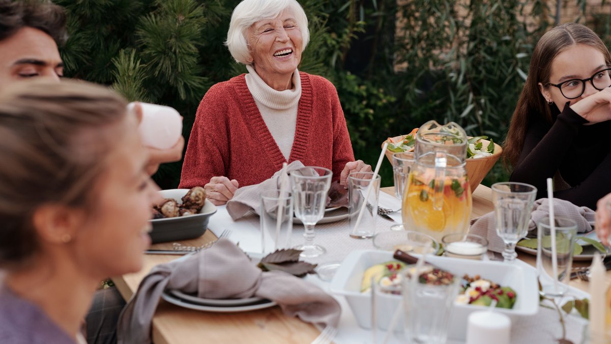 Smiling elderly woman with family and friends enjoying dinner at table backyard garden