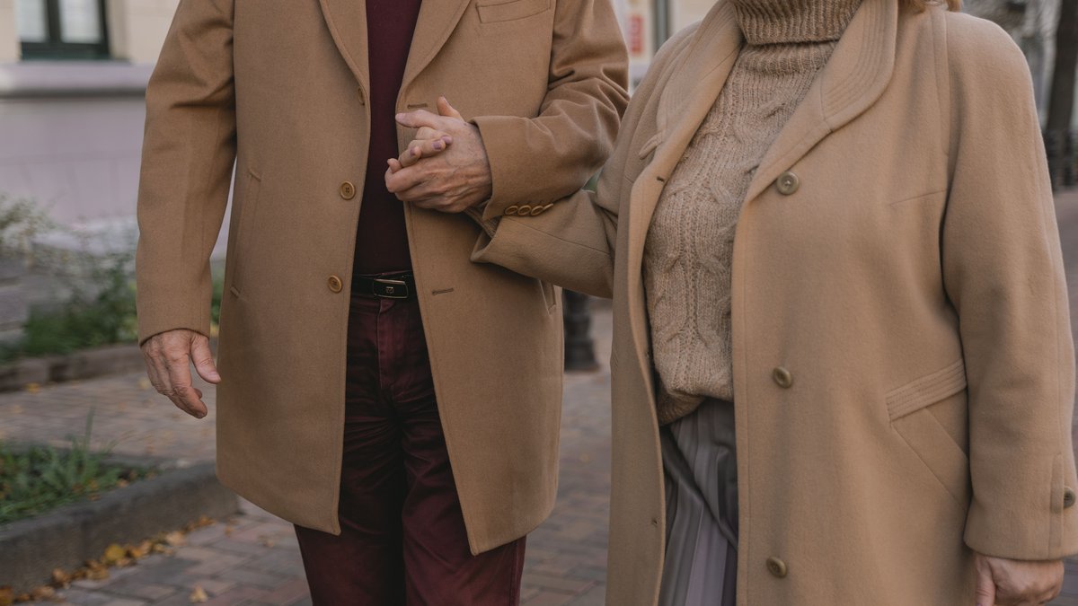 Senior couple holding hands while walking outside in autumn clothing, showcasing love and companionship.