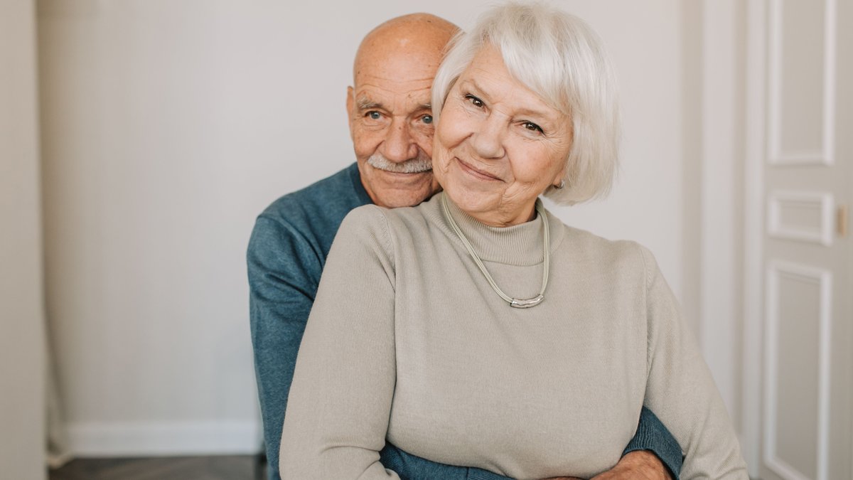 A loving elderly couple hugging indoors, showcasing warmth and happiness.