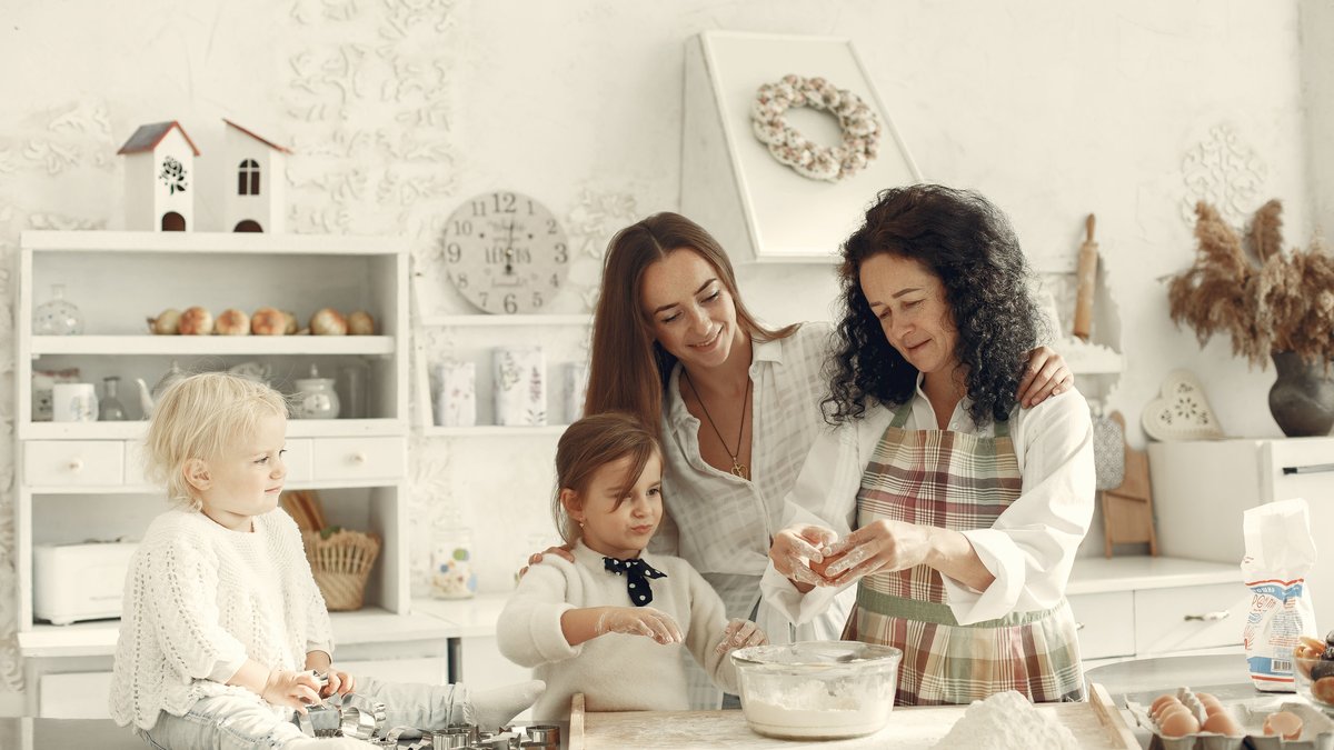 A grandmother, mother, and children baking together in a bright kitchen, enjoying family bonding.