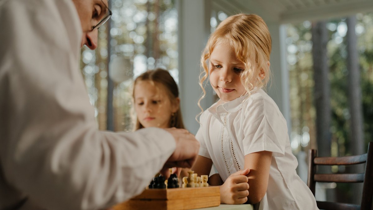 A family moment captured as children and a senior adult enjoy a game of chess indoors.
