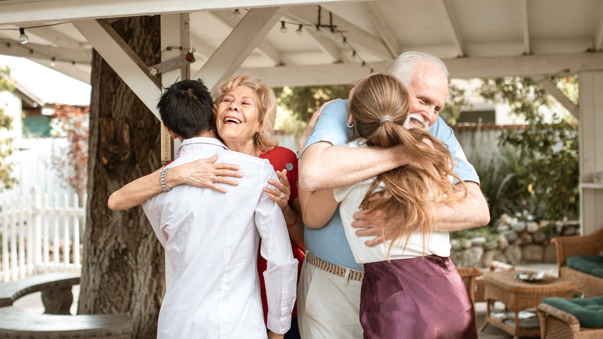 A joyful family reunion outdoors with warm hugs and smiles under a wooden pergola.