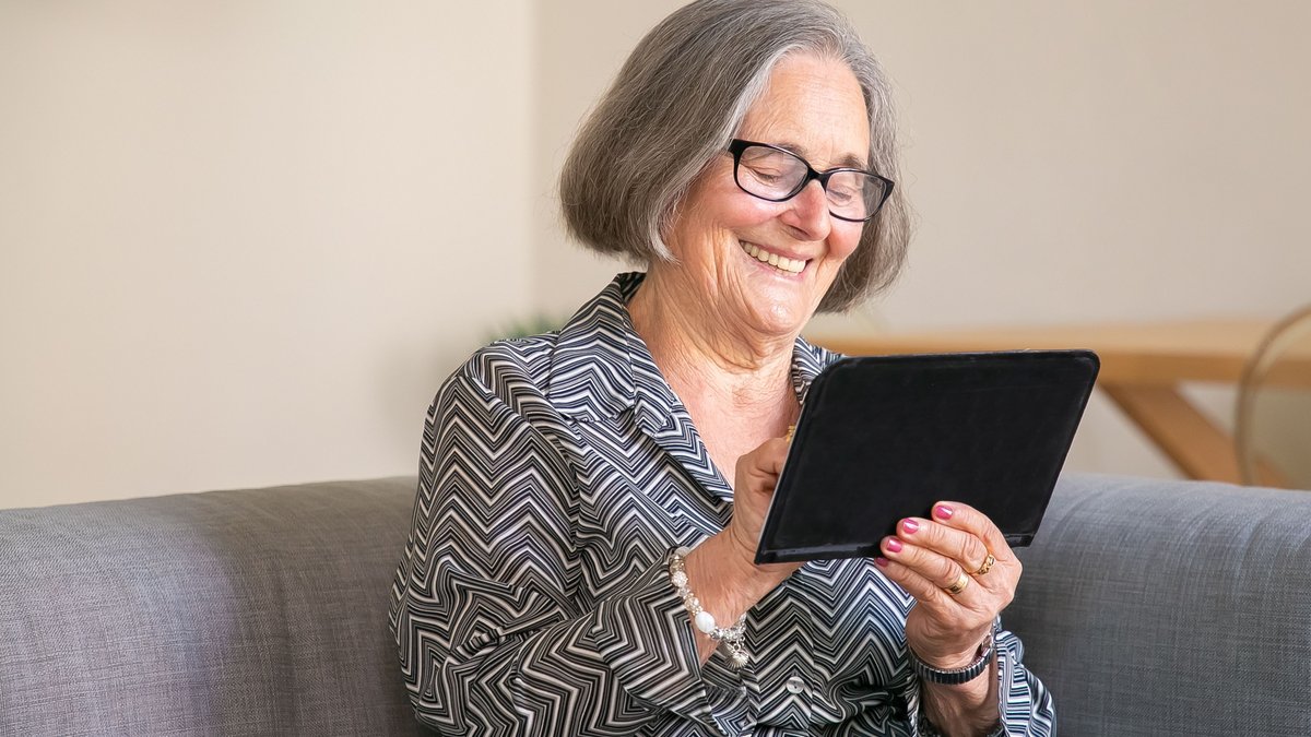 Happy senior woman with gray hair using a tablet at home, enjoying technology.