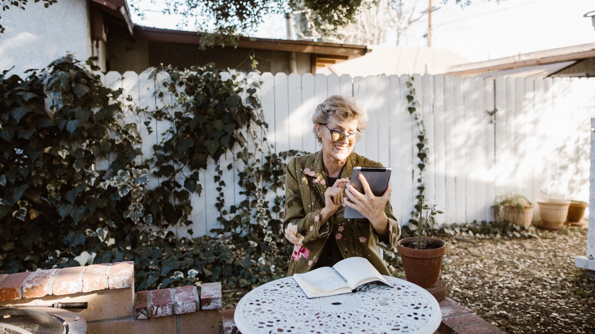 Senior woman enjoying tablet in outdoor garden setting, smiling and relaxed.