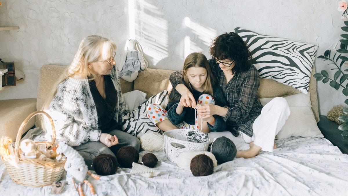 Grandmother, mother, and daughter enjoying knitting together at home. A warm family bonding moment.