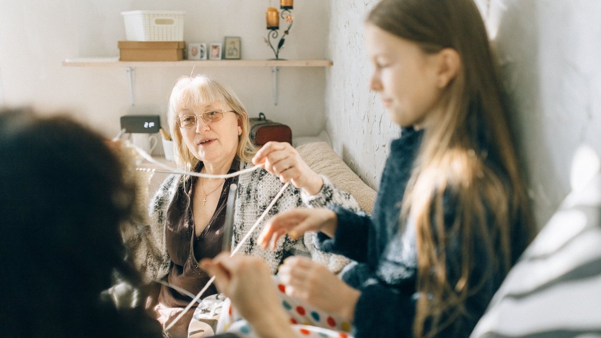 A cozy family moment with grandmother teaching granddaughter crochet indoors.