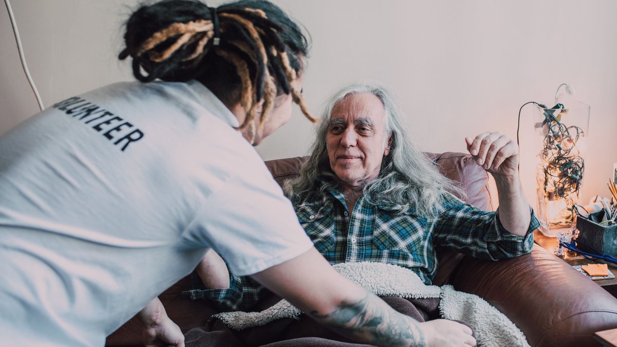 Volunteer helps an elderly man relax at home, promoting charity and care.