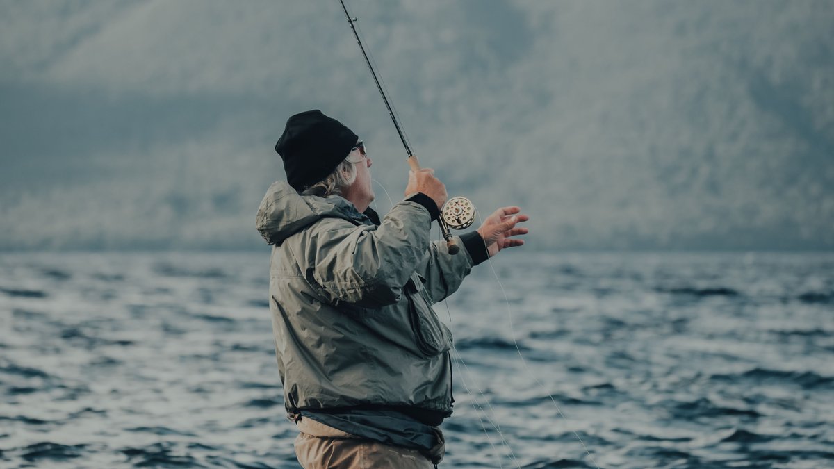 Elderly man enjoys fly fishing at a tranquil lake surrounded by nature.