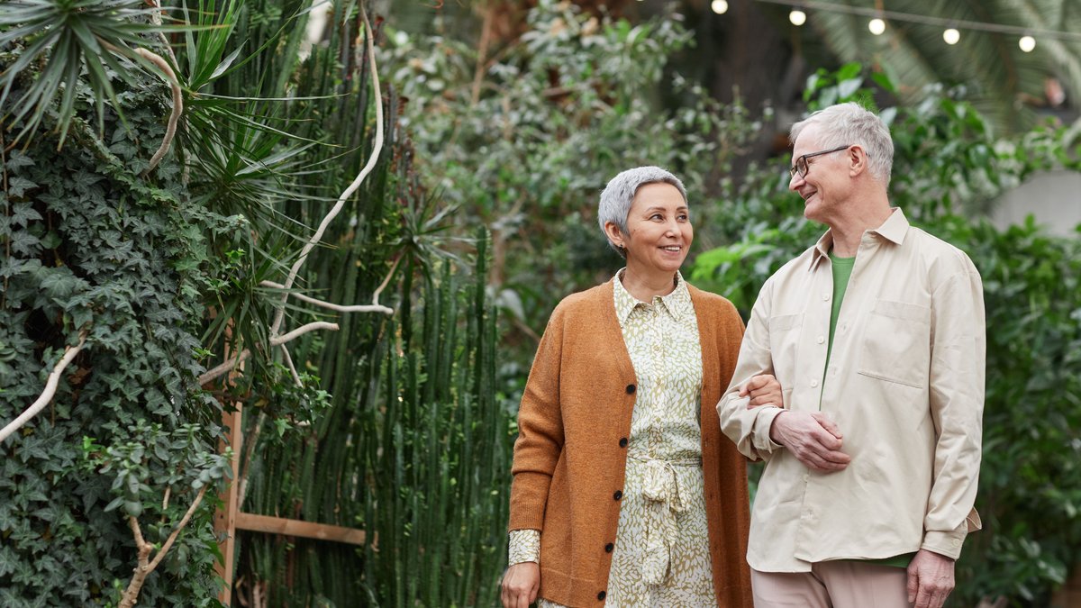 A happy senior couple walking together in a lush greenhouse garden.
