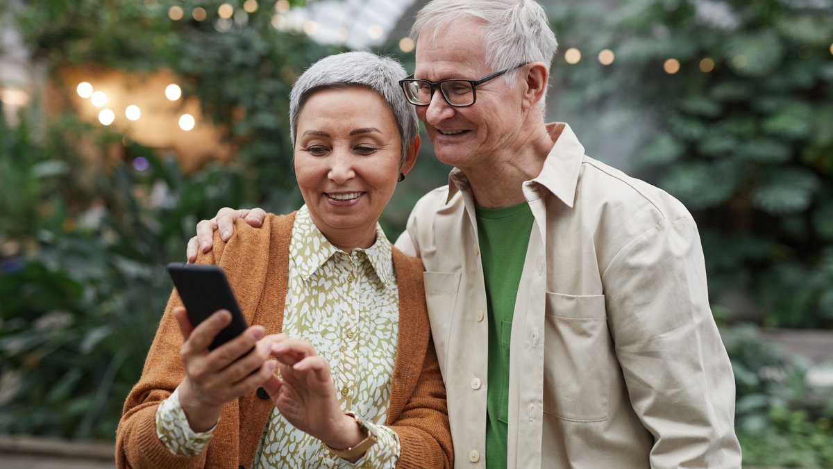 Happy senior couple using a smartphone together outdoors, expressing joy and connection.