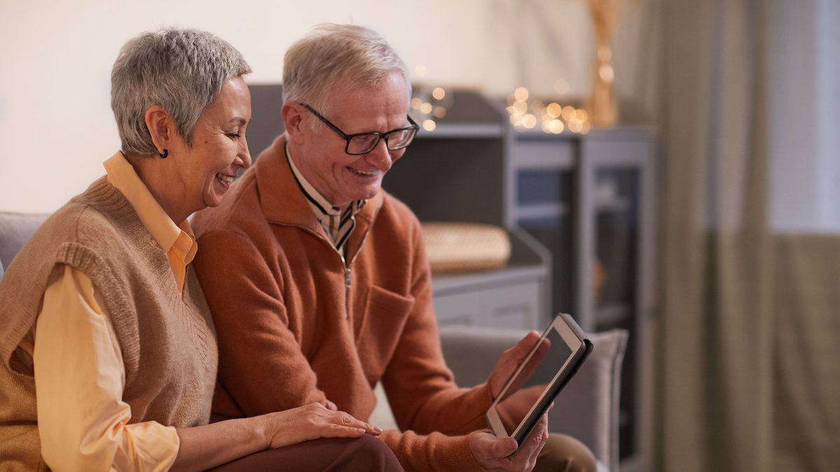 A cheerful senior couple enjoying a video call on a tablet in their cozy living room.