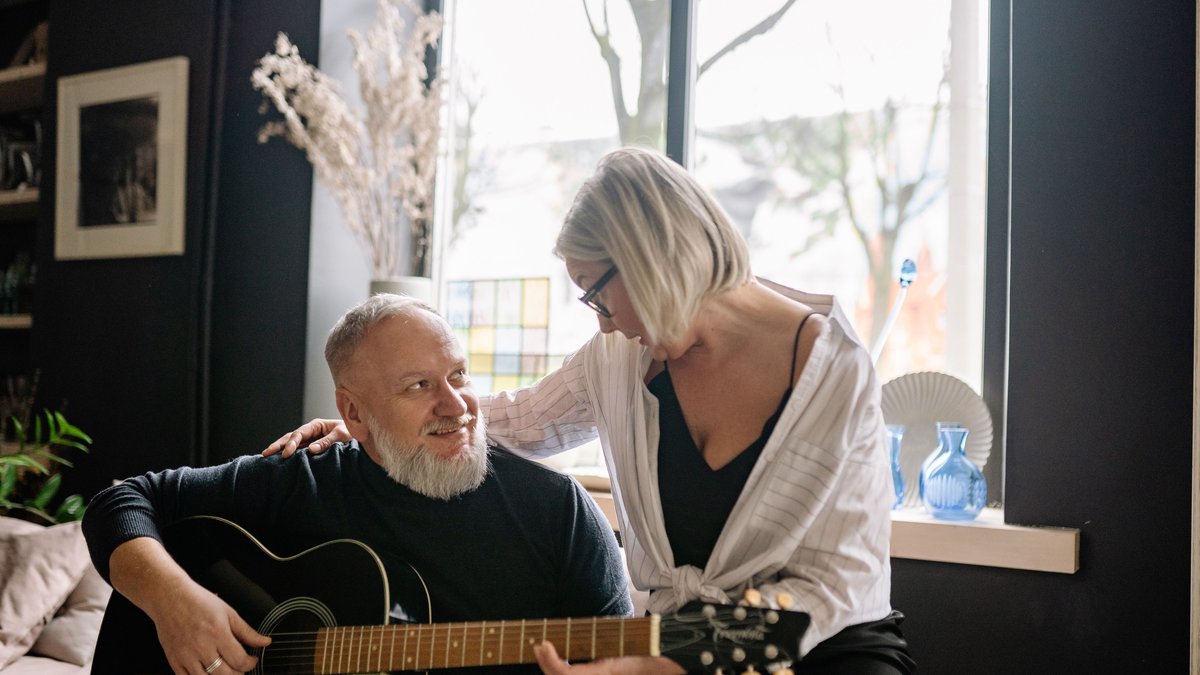 Elderly couple relaxing at home as the man plays an acoustic guitar, radiating warmth and joy.