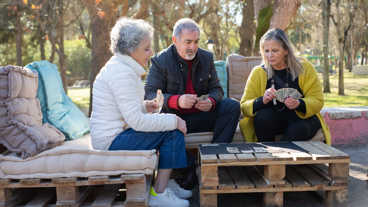 Group of seniors playing cards outdoors, enjoying a relaxing day in Portugal's park.