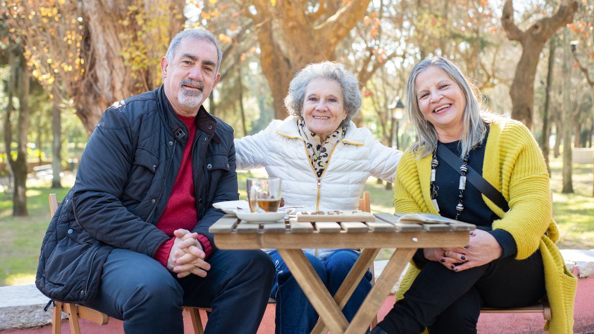 Three smiling seniors together enjoying a sunny day in a park in Portugal.