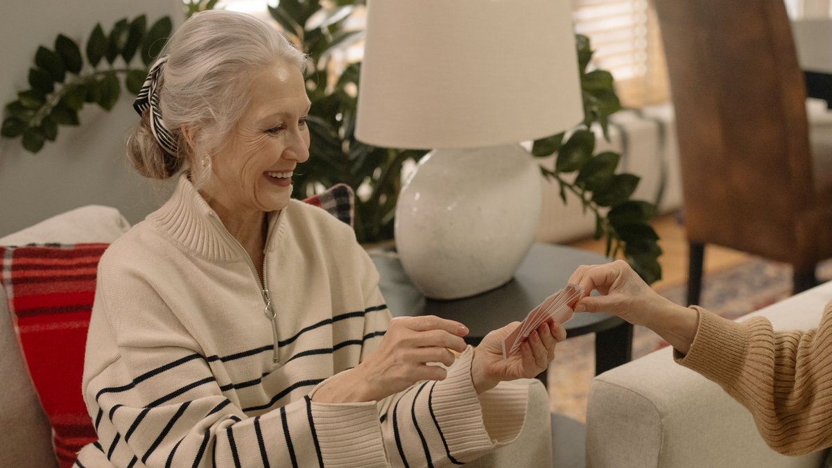 Smiling elderly woman playing a card game indoors, enjoying leisure time.
