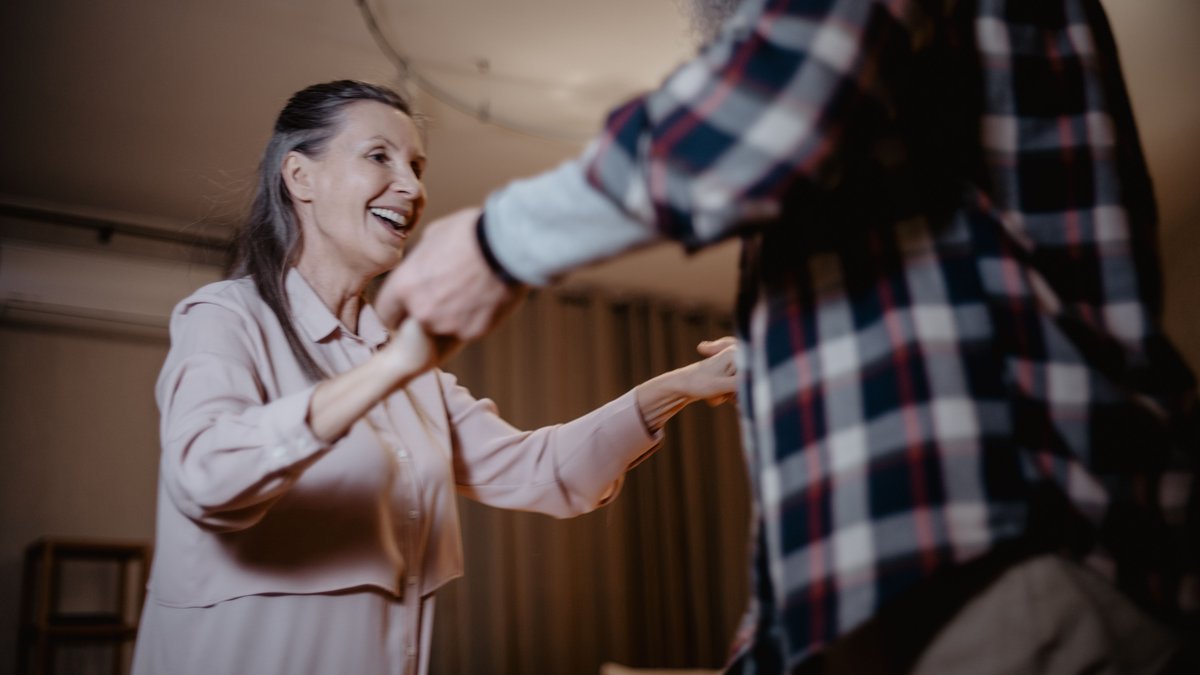 Senior couple enjoying a fun dance together, smiling and holding hands indoors.