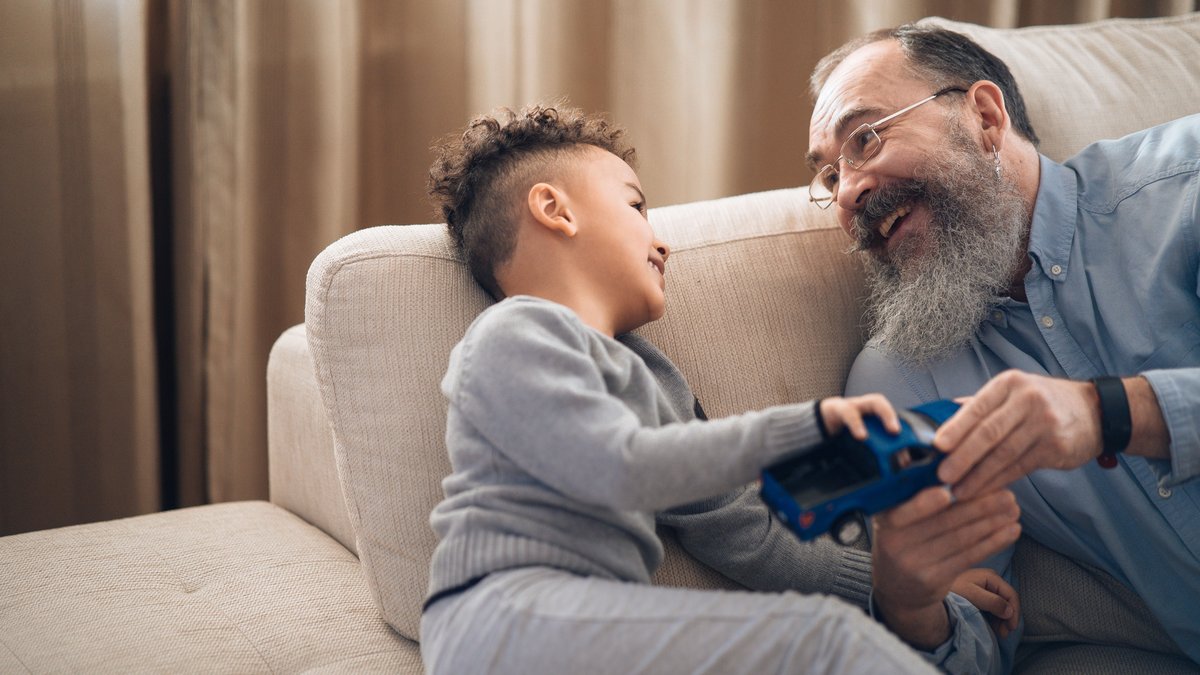 A joyful grandfather and grandson sharing a playful moment on the couch, indoors.
