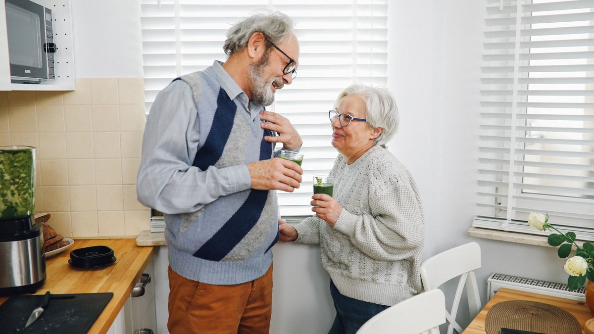 Happy senior couple enjoying refreshing green smoothies together in a cozy kitchen.