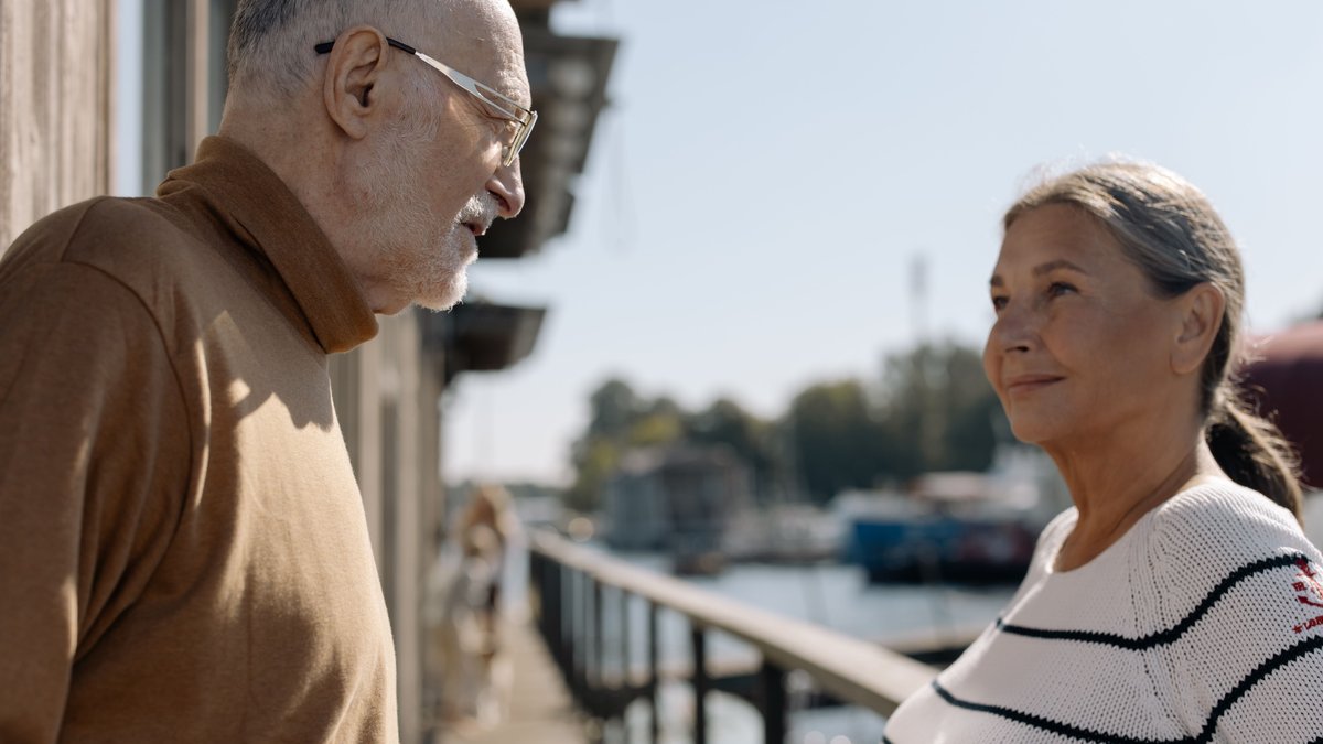Senior couple smiling together by the water on a sunny day, enjoying leisure time.
