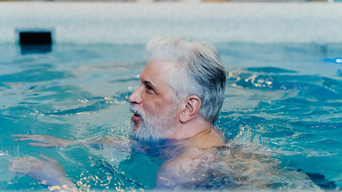 A senior man with grey hair swimming in a pool, enjoying leisure and relaxation.