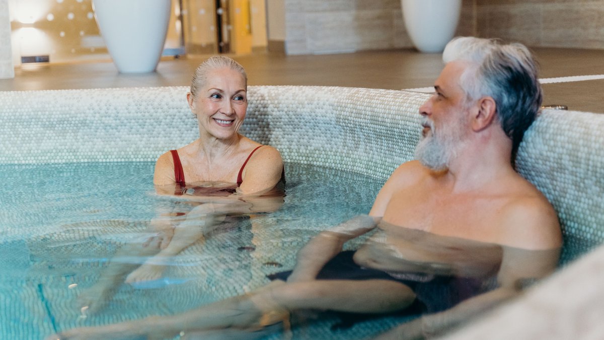 Smiling senior couple relaxing together in an indoor spa pool, enjoying leisure time.