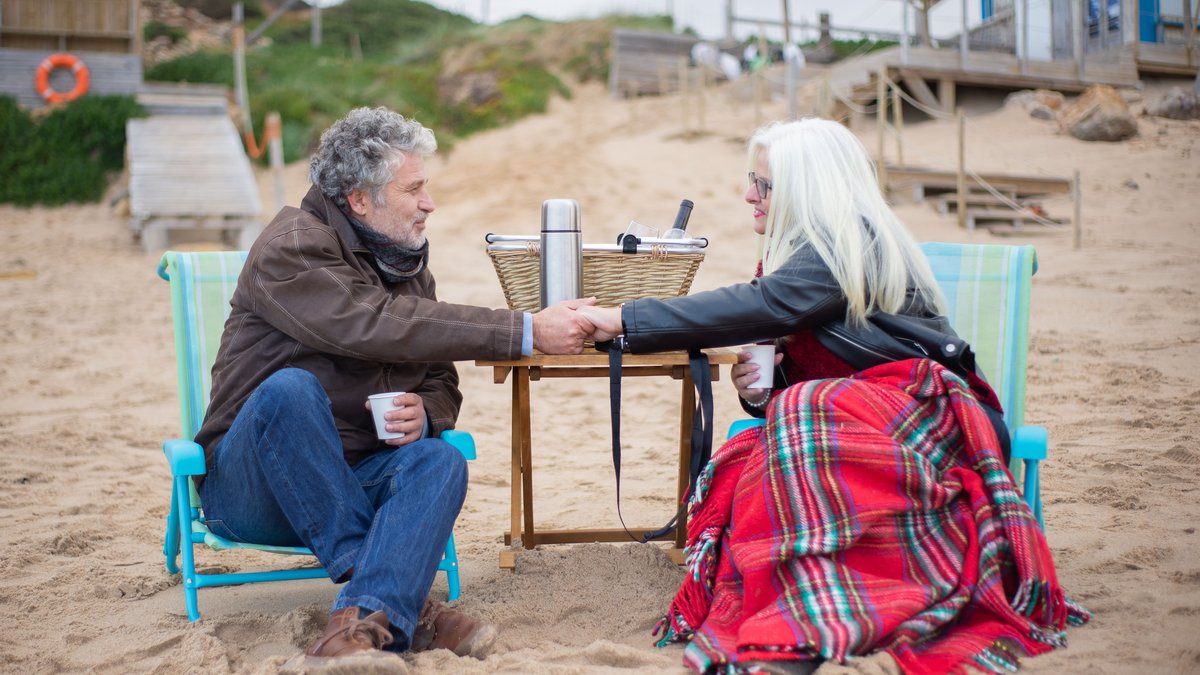 Elderly couple enjoying a romantic picnic by the beach in Portugal, expressing love and happiness.
