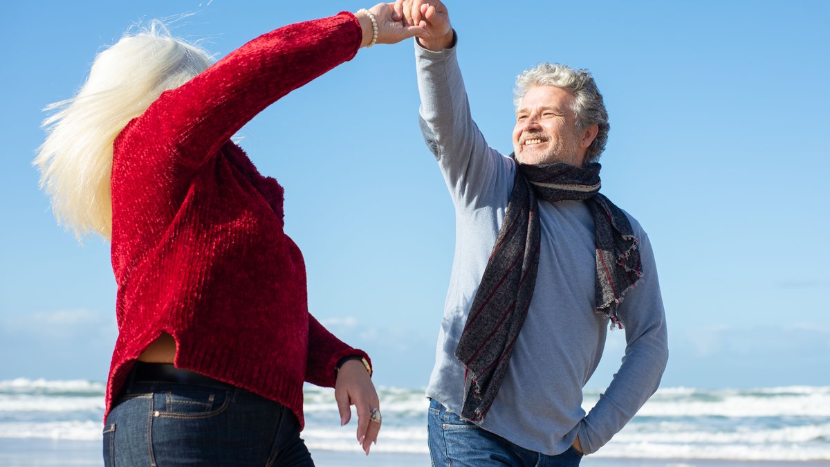 Elderly couple enjoying a dance on a sunny beach, showcasing love and happiness.