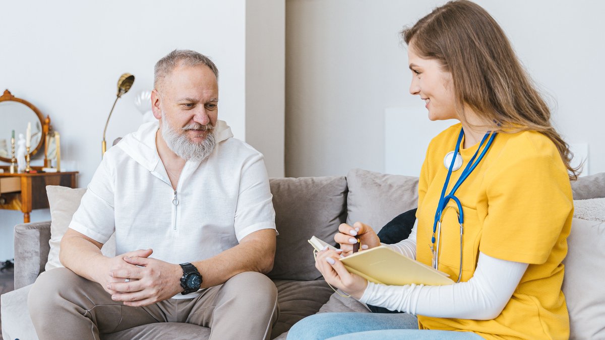 A healthcare professional smiles while consulting with an elderly man in a cozy indoor setting.