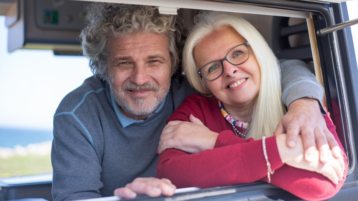 Cheerful senior couple enjoying a sunny day together, smiling and embracing in a car window.