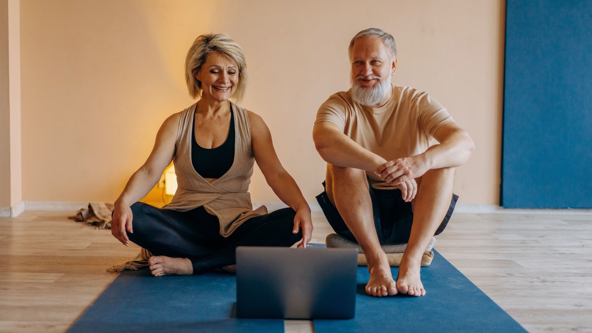 An elderly couple practicing yoga at home with online guidance, smiling and relaxed.