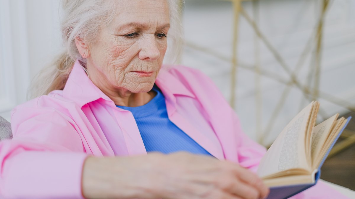 Elderly woman relaxing indoors, enjoying a quiet moment with a book.