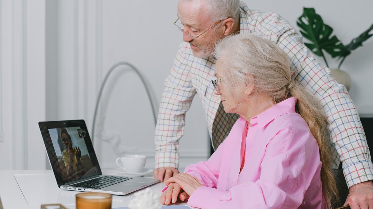 Elderly couple enjoying a video call on their laptop at home, showcasing family connection technology.