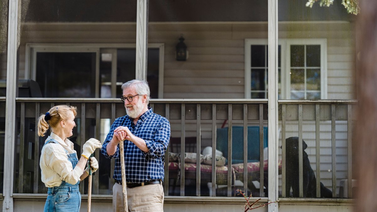 Senior couple gardening outside their home, enjoying a sunny day together.