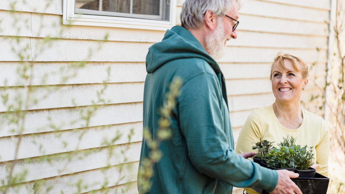 Smiling elderly couple gardening together outdoors, enjoying horticulture as a hobby.