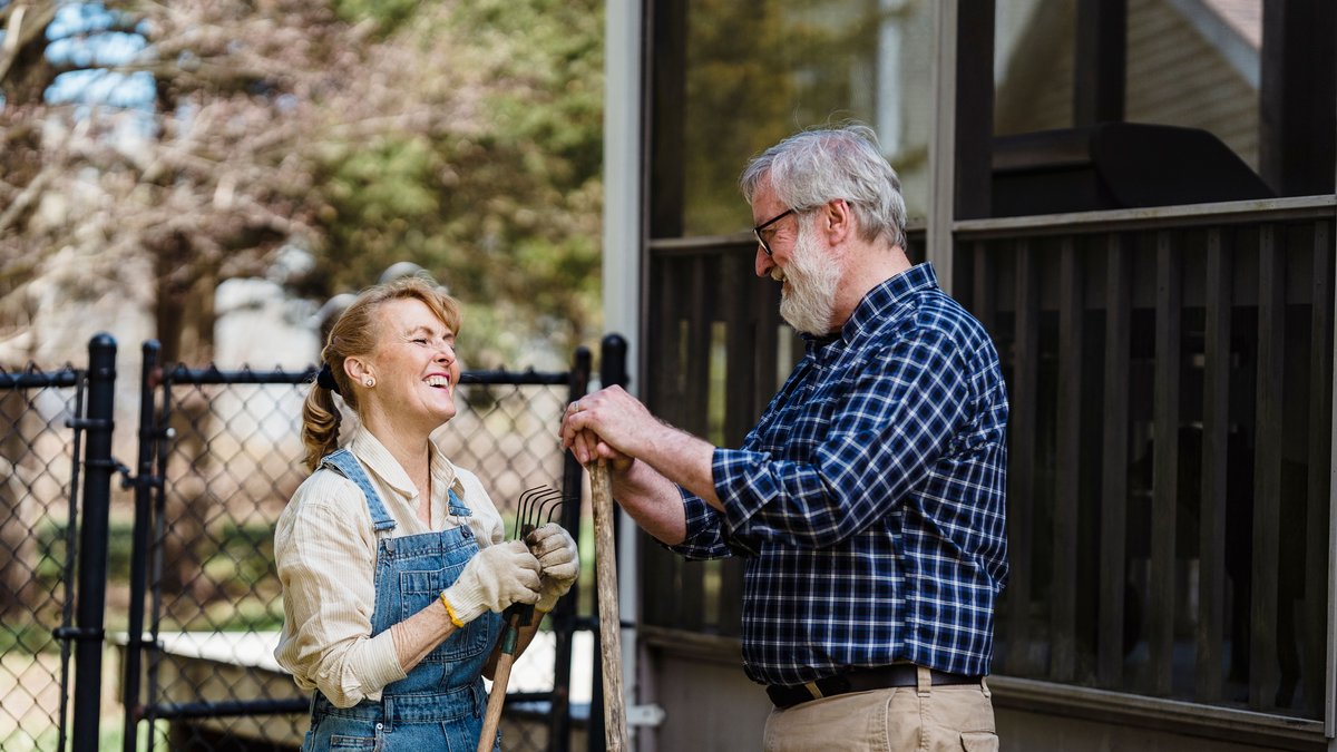Elderly couple enjoying gardening in their backyard on a sunny day, filled with smiles and joy.