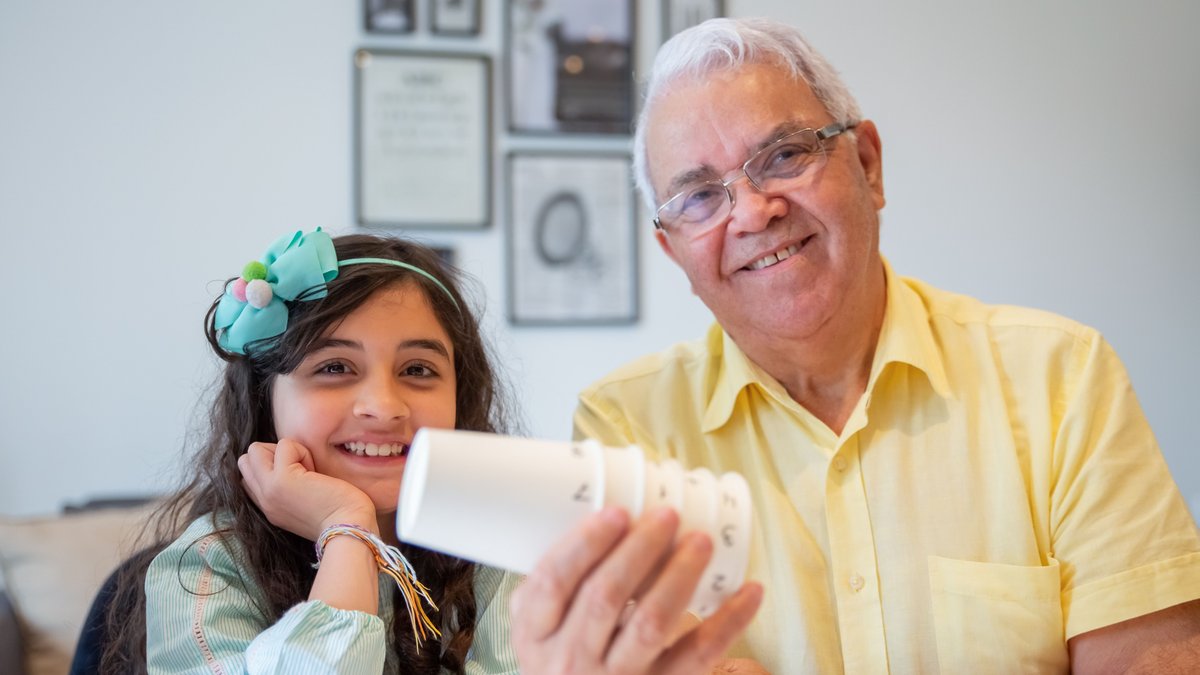 Smiling grandfather and granddaughter enjoying time together with playful cups indoors.