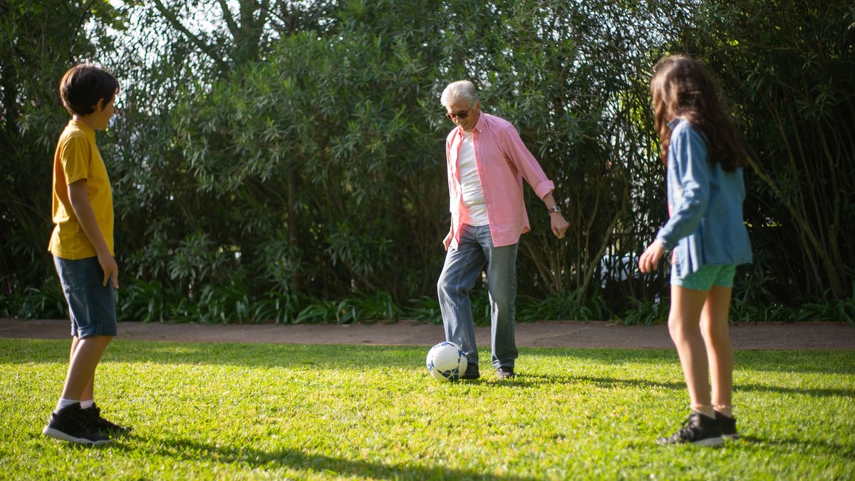 A joyful moment of a grandfather playing soccer with his grandchildren on a sunny day.