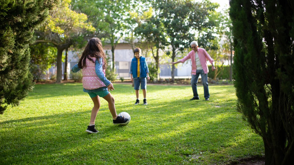 A grandfather playing football with his grandchildren in a sunny park, enjoying quality time outdoors.