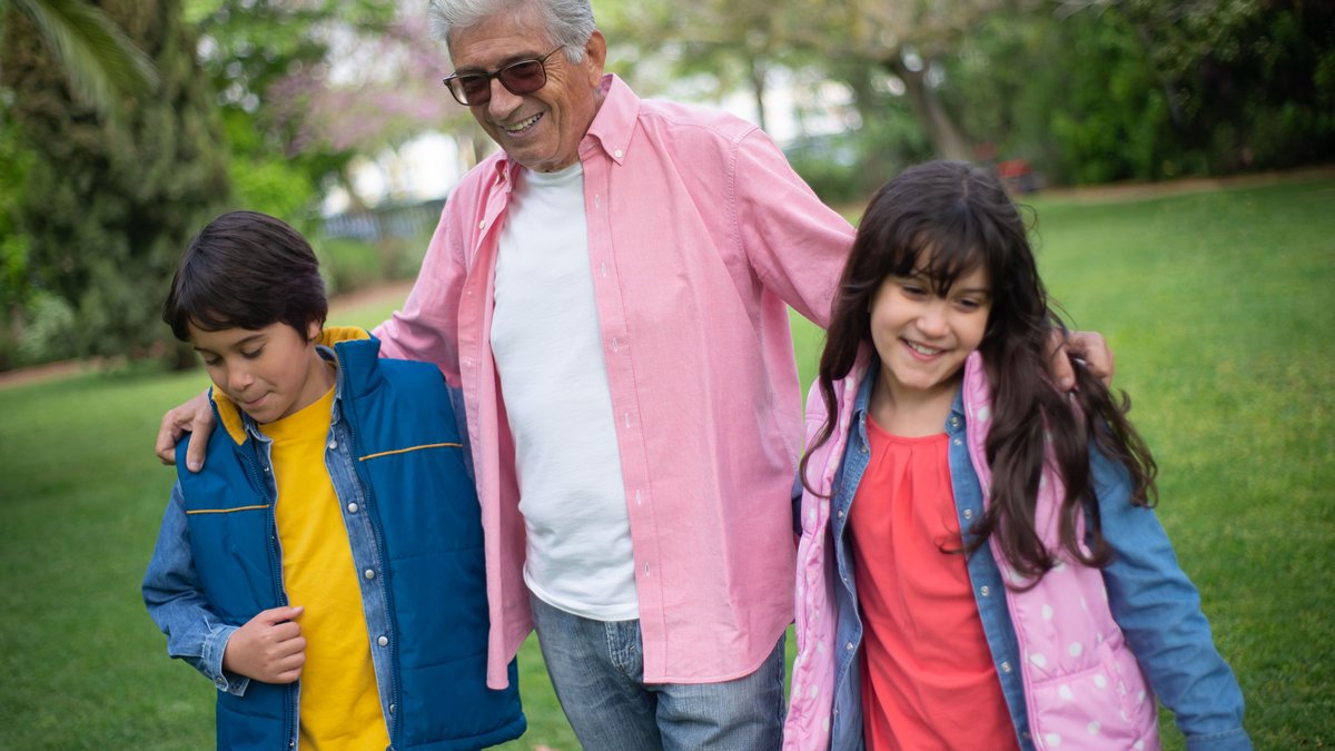 Happy grandfather bonding with grandchildren in a lush park, enjoying a joyful day outdoors.