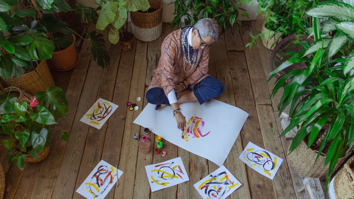 Senior woman enjoys painting surrounded by indoor plants, showcasing creativity and leisure.