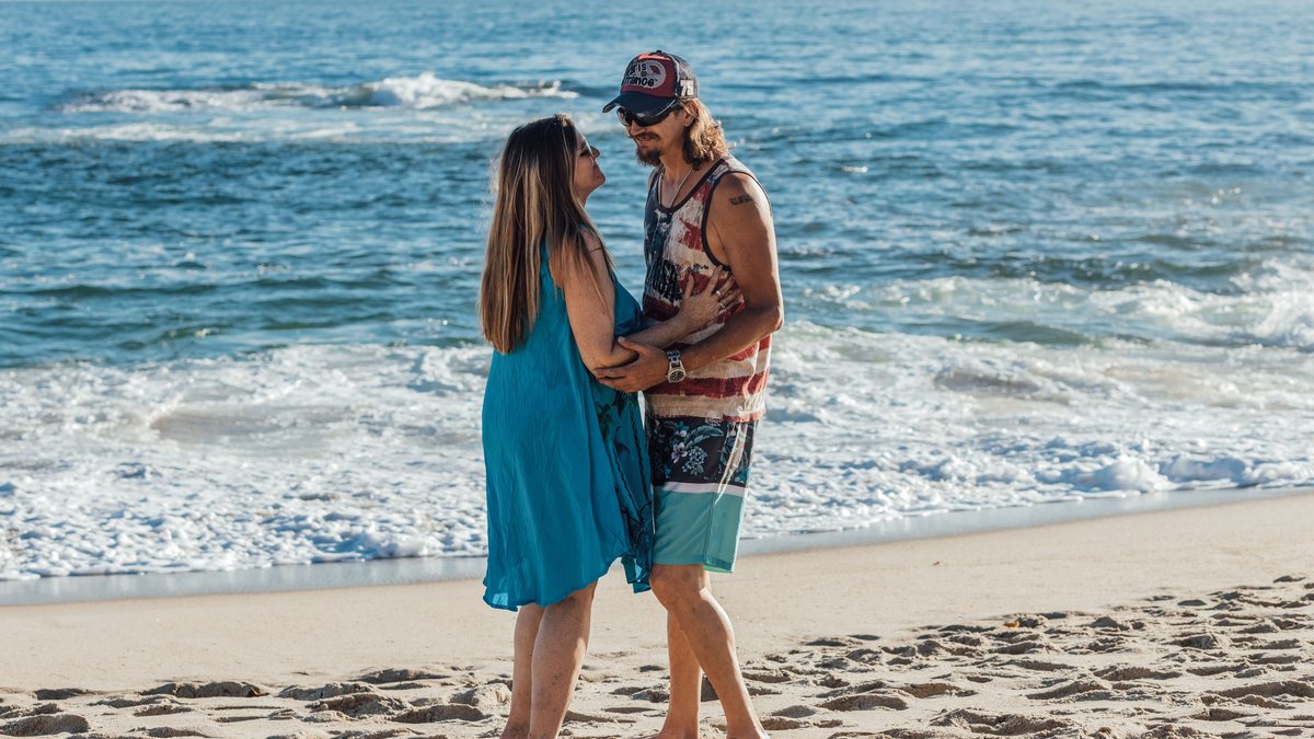 Senior couple enjoys a romantic stroll on a sunny beach, embodying love and relaxation.