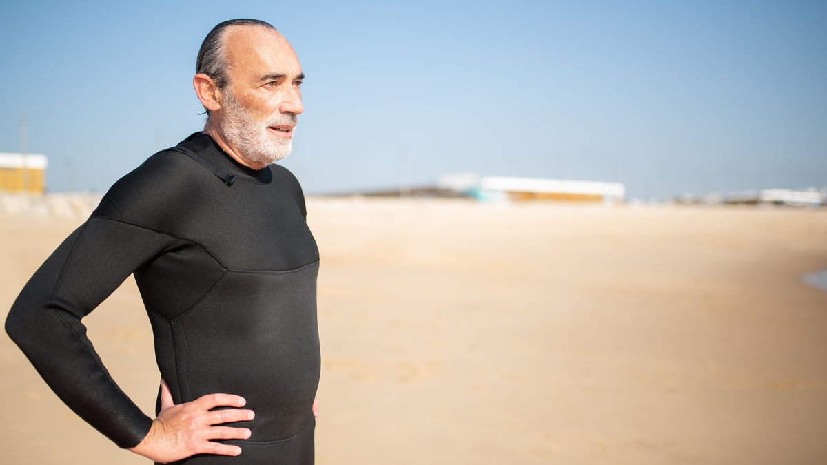 Elderly man in a wetsuit enjoying a sunny day on a Portuguese beach, ready for a swim or surf.