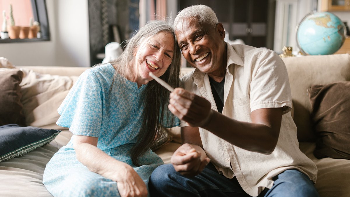 Joyful senior couple sharing a joint on a cozy sofa, enjoying their time together.