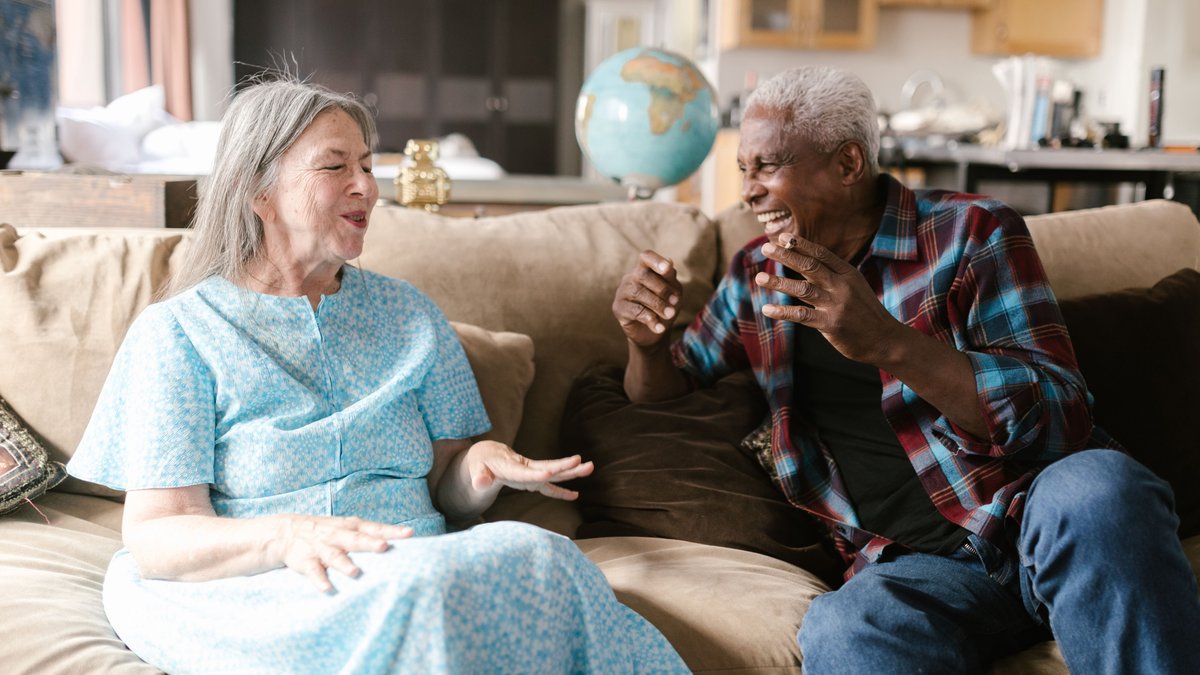Senior couple laughing together on a cozy sofa, enjoying a joyful conversation indoors.