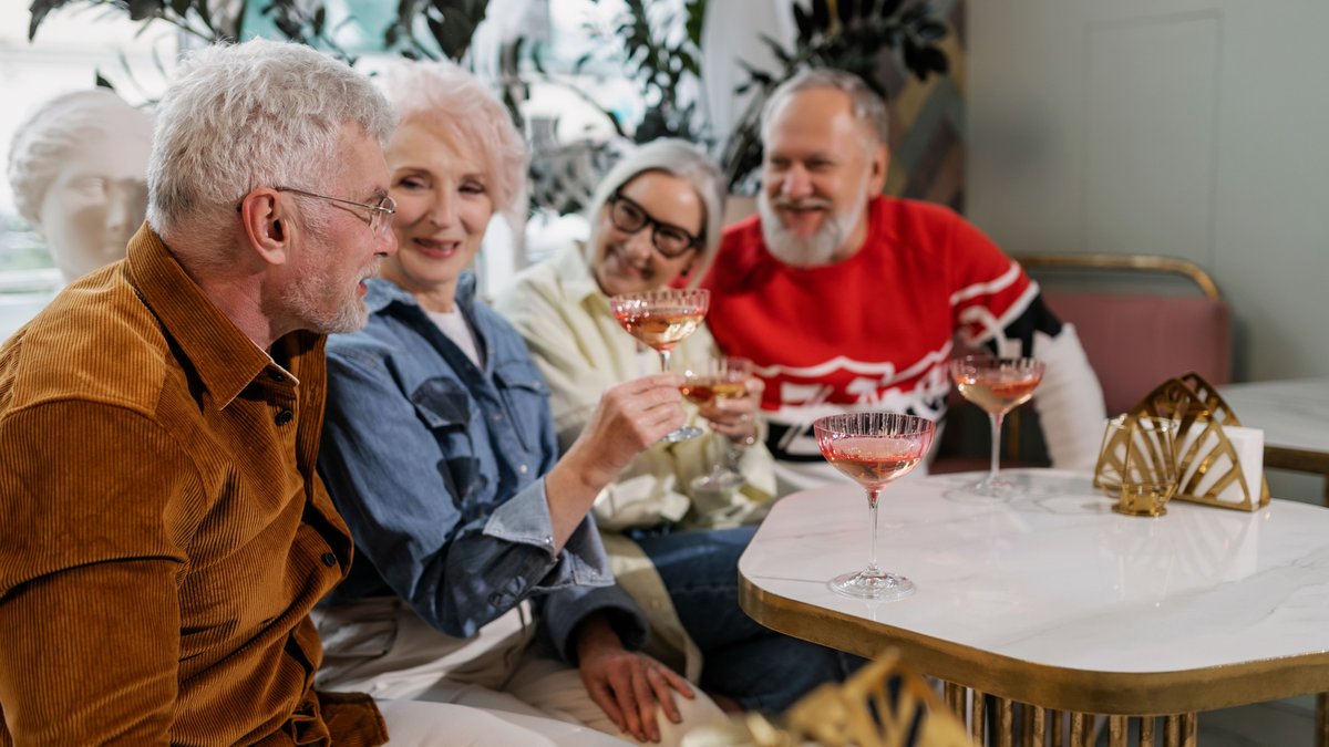 Senior friends enjoy a cheerful indoor gathering, sharing drinks and laughter.