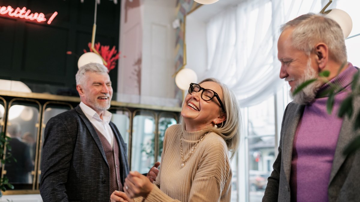 Three senior adults laughing and enjoying a lively indoor gathering, creating a joyful atmosphere.