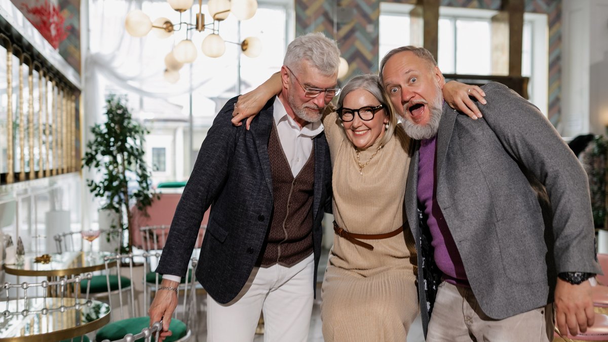 Elderly friends laughing and hugging at a lively indoor café setting, showcasing friendship.