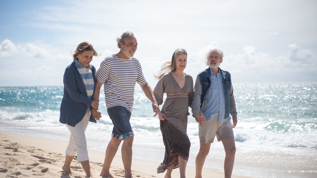 Happy senior couples walking along a sunny Portuguese beach, enjoying a leisurely day by the sea.