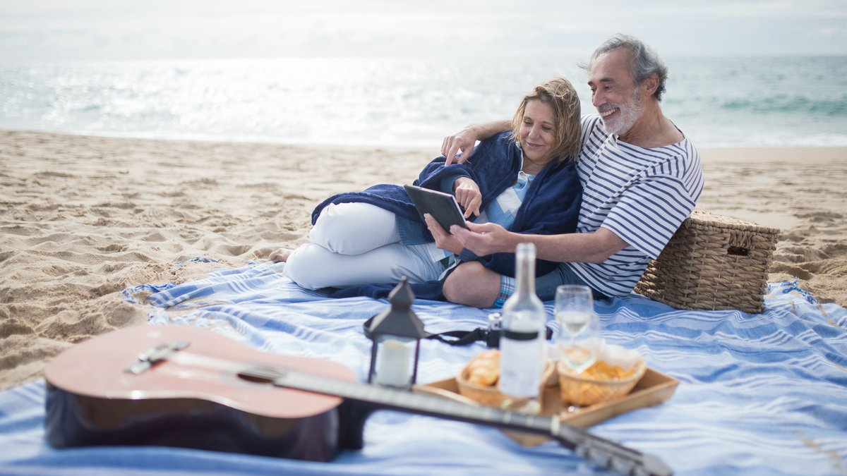 A happy senior couple enjoys a beach picnic in Portugal, embracing leisure and relaxation.